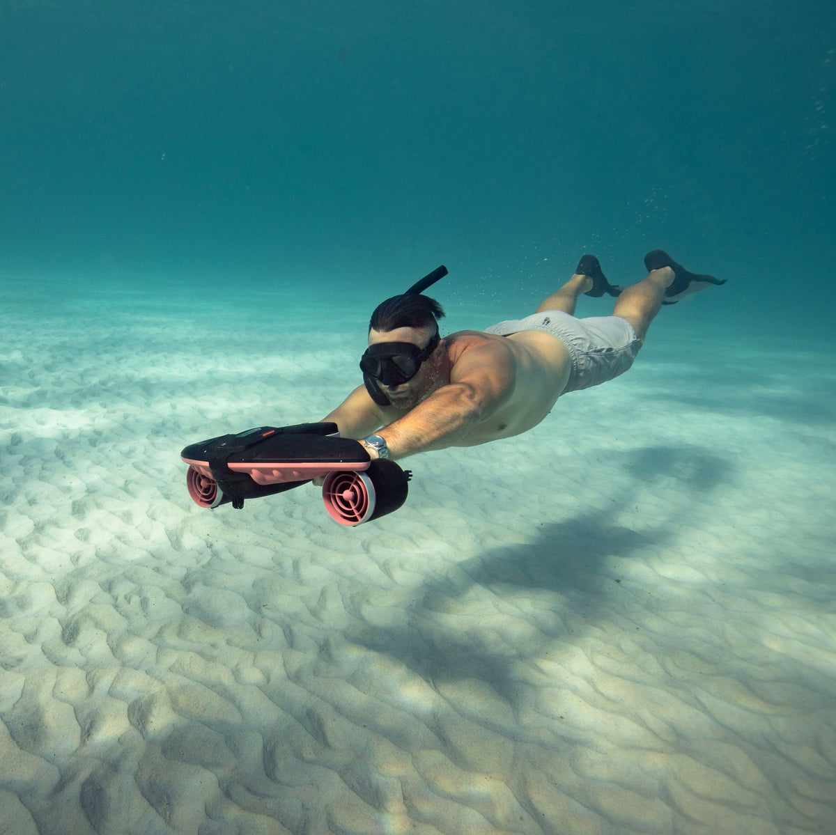 Swimmer holding a red Sublue Navbow scooter above a sandy seabed